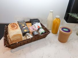 A basket with bread, cheese, butter, sweets, jam, and drinks on a countertop at Duke's Barn in Blackawton near Dartmouth
