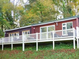 A wooden cabin with a deck surrounded by trees at I C Lundy Too Bideford Bay Holiday Park near Clovelly