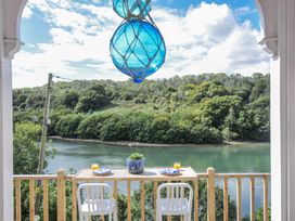 An outdoor balcony with a table and chairs overlooking a river at Mayhurst Looe