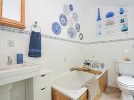 A bathroom with a bathtub, sink, shelf, and decorative items at Mayhurst in Looe