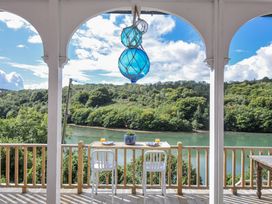 An outdoor balcony overlooking a river with chairs and a table at Mayhurst in Looe