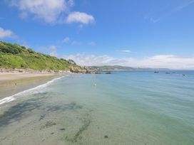 A beach with people in the water and boats near rocks at Mayhurst in Looe