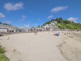 A beach with people and houses on a hill at Mayhurst in Looe