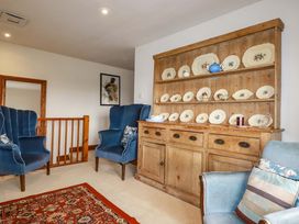A sitting room with blue armchairs and a wooden shelf with dinnerware at Rosewin Farmhouse near St Minver