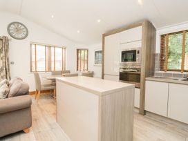 A kitchen with a table, chairs, and a wall clock at Easedale Lodge, Waterside Wood 2, White Cross Bay near Windermere