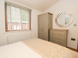 A bedroom with a bed, wardrobe, mirror, and chest of drawers at Easedale Lodge, Waterside Wood 2, White Cross Bay near Windermere