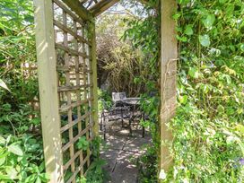 A garden area with a table and chairs under a trellis at Honey Cottage in Ilfracombe