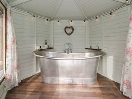 A bathroom with a silver bathtub and wine bottle on a shelf at Y Cwlwm in Lampeter