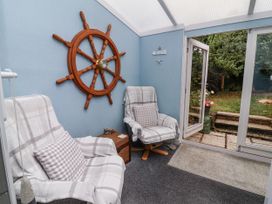 A conservatory with armchairs and a wheel decoration at Ocean Cottage in Bude