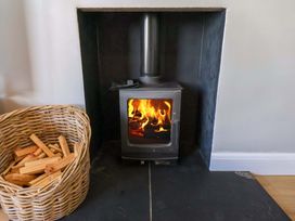 A wood stove with fire and a basket of firewood in a living room at Floraville