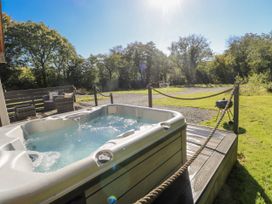 A hot tub on a deck with outdoor seating and a barbecue grill at Dwrgi Llanybydder