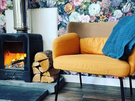 A living room with a stove, chair, and firewood at Hen Stablau Dinmael near Cerrigydrudrion