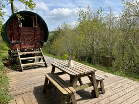An outdoor seating area with a wooden table and benches beside a gypsy caravan at Goldfinch in Panson Mill near Ashwater