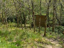 A wooded area with a wooden structure surrounded by trees at Goldfinch in Panson Mill near Ashwater