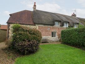 A garden with a thatched roof cottage and hedges at Bubbs Cottage
