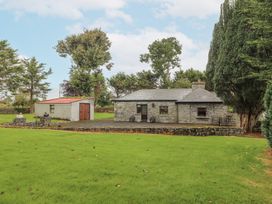 A stone house with a green lawn and a shed at Coole Gate Lodge Gort, County Galway