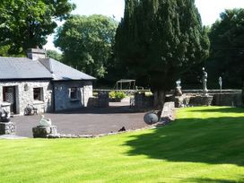 An outdoor area with a stone house, garden, and a swing set at Coole Gate Lodge, Gort, County Galway