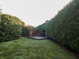 A garden with a wooden deck and chairs at Wellinghill Cottage at Wellinghill House Charlton Kings