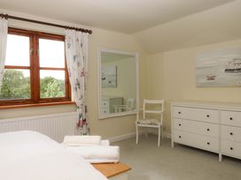 A bedroom with a window, mirror, chair, and chest of drawers at The Milking Shippon at Thorne in Langtree near Great Torrington