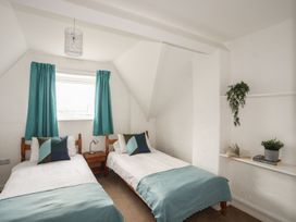 A bedroom with two beds, a window, and a shelf at Fadrun - 3 Ty'n Don