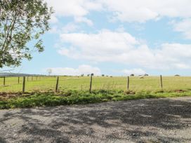 A grassy field with a fence and trees at Bluebell Cottage