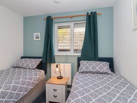 A bedroom with two beds, a lamp, and a window at Mayfly Lodge St Tudy