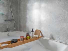 A bathtub with a bamboo tray and various personal care items at Newlands in Yelverton