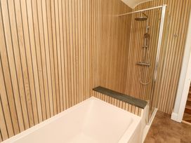 A bathtub and shower area with wooden paneling at East View in Kirkby Stephen
