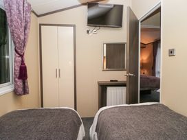 A bedroom with two beds, a wardrobe, and a television at Feather Hill Lodge in Windermere