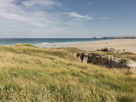 View of the beach and ocean with grass and rocks at Teach Tra East in Perranporth