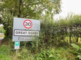 A speed limit sign indicating 30 mph for Great Corby near a road in Great Corby