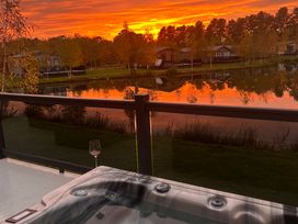 A hot tub with a glass beside it overlooking water and trees at Lakewood Retreat in Woodhall Spa