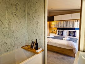 A bathroom with a bathtub and a bedroom with a bed at Hotchkin Lodge in Woodhall Spa