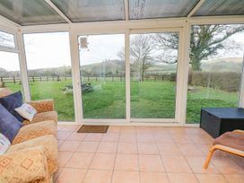 A conservatory with a sofa and views of grass and trees at Court House Farmhouse in Charmouth