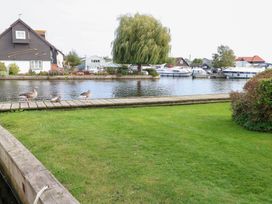 A view of a house next to a river with ducks on a dock and boats in the background at Cotman Cottage, Norwich