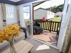 A living room with a view of a deck and flowers in a vase at Stag Lodge, Caravan 70 Great Yarmouth