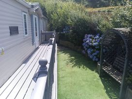 A garden area with decking, a bench, and flowers at Clarach Bay Holiday Village - Holiday Accommodation 10536 Aberystwyth