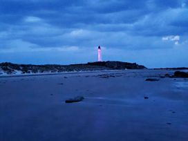 a lighthouse illuminated at dusk on a sandy beach at Silver Sands Holiday Park - Holiday Accommodation 11481 in Lossiemouth