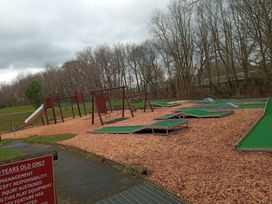 A playground with a slide and swings in a wooded outdoor area at Penlan Holiday Park - Holiday Accommodation 11792, Cenarth