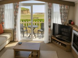 a living room with a TV, coffee table, and view of a patio at Freshwater Beach Holiday Park - Holiday Accommodation 12281 in Burton Bradstock