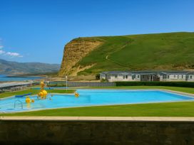 a swimming pool with a grassy area and hillside in the background at Freshwater Beach Holiday Park - Holiday Accommodation 12281 in Burton Bradstock
