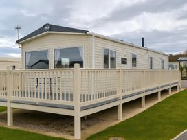 A mobile home with a deck and table at Reighton Sands Holiday Park - Holiday Accommodation 14875 Filey