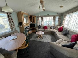 a lounge area with a curved sofa and a circular dining table at Coral Beach - Holiday Accommodation 16858 in Ingoldmells