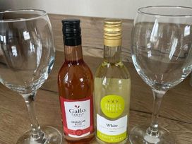 two wine glasses next to two bottles of wine on a wooden surface at Quay West Holiday Park - Holiday Accommodation 16905, New Quay