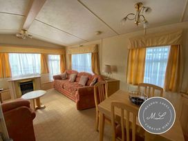a living room with a sofa, chairs, table, and windows at Meadow Lakes Caravan Hire