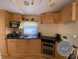 a kitchen with wooden cabinets, a countertop, and appliances at Meadow Lakes Caravan Hire