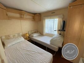 a bedroom with two beds, a window, and storage units at Meadow Lakes Caravan Hire