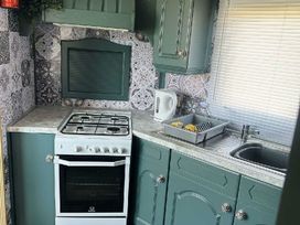 a kitchen with green cabinets, a gas stove, and a sink at Hafan y Mor Haven - Holiday Accommodation 18358, Pwllheli