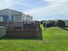 a mobile home with a wooden deck and grassy area at Hafan y Mor Haven - Holiday Accommodation 18358 Pwllheli