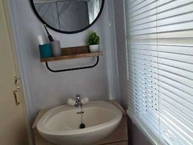 a bathroom with a sink and round mirror at Hafan y Mor Haven - Holiday Accommodation 18358 in Pwllheli
